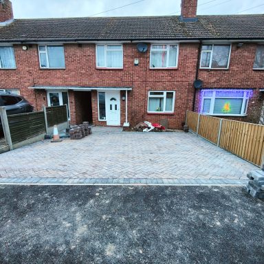 Paved driveway in front of a red brick terraced house with wooden fencing.