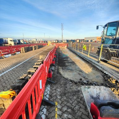 Construction site with barriers, machinery, and ongoing roadworks under a clear blue sky.