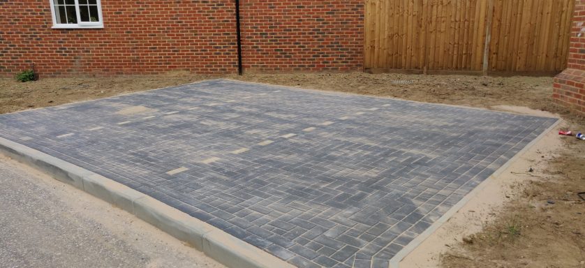 Paved driveway with a partially completed surface and surrounding bare soil.