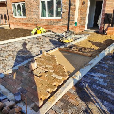 Construction workers laying paving stones on footpaths and driveways outside new houses.