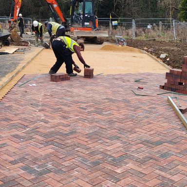 Workers laying block paving on a construction site.