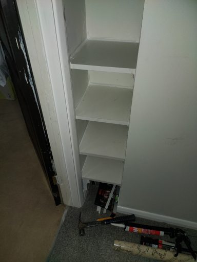 A narrow, empty shelf unit with four shelves against a wall.